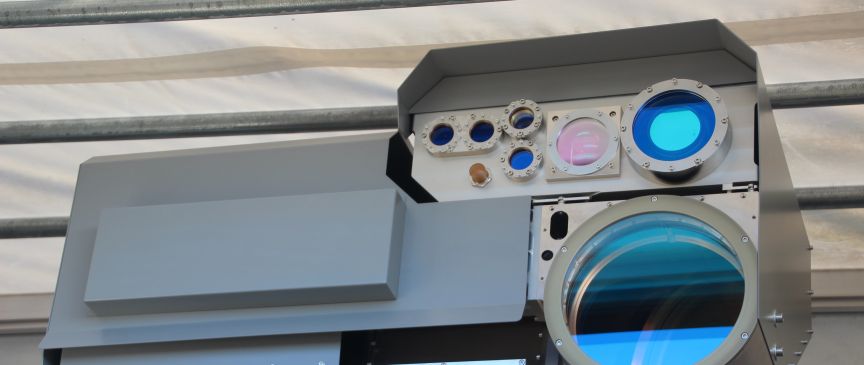 Graues militärisches Gerät mit mehreren optischen Linsen und Sensoren, montiert unter einem Vordach.