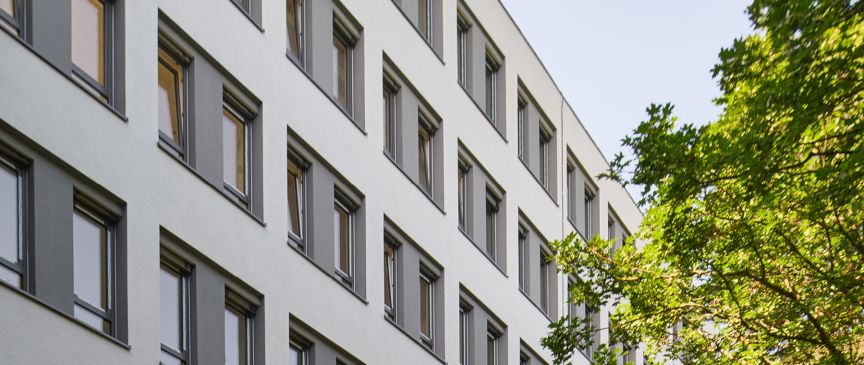 Weißes Bürohaus mit vielen Fenstern und ein Baum