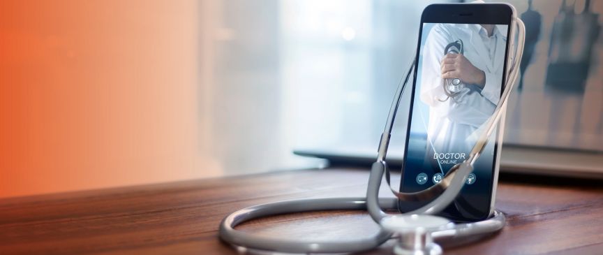 Smartphone mit Arzt-App auf Holztisch, umgeben von einem Stethoskop. Auf dem Display: "Doctor Online".