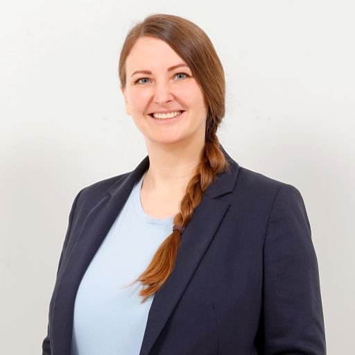 Frau mit geflochtenem roten Haar und blauem Blazer lächelt vor hellem Hintergrund.