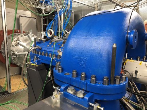 Blaue Industriemaschine mit Flanschverbindungen, Bolzen und Kabeln in einem technischen Raum mit Metallgehäusen.