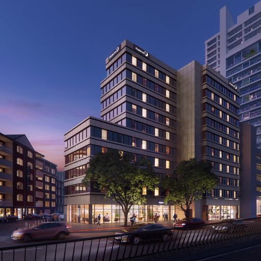 Modernes mehrstöckiges Hotelgebäude mit Premier Inn-Logo bei Nacht, beleuchtet, umgeben von Straße und Bäumen.
