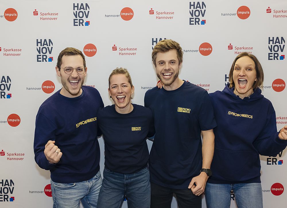 Vier Personen in dunkelblauen Sweatshirts posieren lächelnd vor einem Sparkasse-Hannover-Banner.