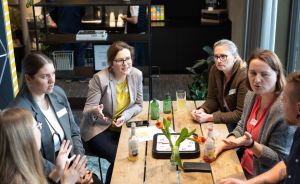 Vier Frauen sitzen an einem Holztisch und diskutieren. Auf dem Tisch stehen Getränke und Tulpen.