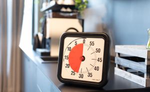 Quadratischer schwarzer Time Timer auf einer dunklen Ablage, rotes Segment zeigt ca. 30 Minuten verbleibende Zeit an.