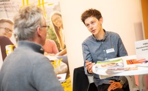 Zwei Männer sitzen an einem runden Tisch im Gespräch. Im Hintergrund ein Banner der Hochschule Hannover.