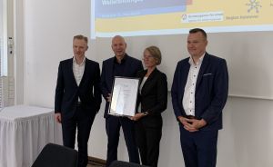 Vier Personen stehen vor einer Präsentation „Weiterbildungspreis 2024". Zwei halten gemeinsam eine gerahmte Urkunde.