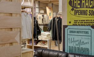 Schwarzes Ledersofa in einem Urban Outfitters Store, dahinter Kleiderständer und Werbeplakate für Den Haag und Madrid.