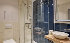 Modernes Badezimmer mit Glasdusche, Wandhänge-WC, Waschtisch mit Aufsatzbecken und blauen Wandfliesen.