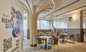 Hotelrestaurant mit runden Tischen, grauen Stühlen, Holzsäulen-Skulptur und Werbebanner "JuneSix Hotel Hannover".