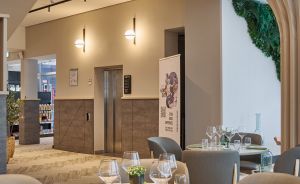 Modernes Restaurant mit runden Marmortischen, grauen Stühlen, Weingläsern, grünen Servietten und geschwungenen Holzrippen an der Decke.