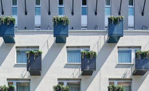 Mehrstöckige Gebäudefassade mit gleichmäßig angeordneten Balkonen, blauen Geländern und begrünten Blumenkästen.