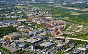 Luftaufnahme einer Stadt mit Gewerbegebiet, Wohnhäusern, Baustellen, Feldern und grünen Freiflächen.