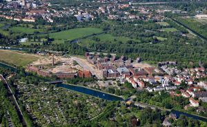 Luftaufnahme einer Stadt mit Kanal, Industriegebäuden, Wohnhäusern, Grünflächen und Kleingärten.