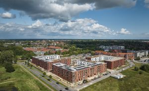 Luftaufnahme eines Stadtviertels mit roten Backsteingebäuden, Solaranlagen auf Dächern, Straßen und grüner Umgebung.