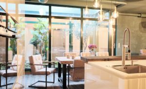 Modernes Café mit Küchentheke, Pendelleuchten, Industrierohren an der Decke, Sitzbereichen und großen Fensterfronten.