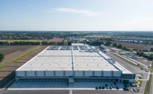 Luftaufnahme eines großen Lagergebäudes mit Solarpanelen auf dem Dach, umgeben von Feldern und einer Kleinstadt.