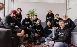 Gruppe von 10 Personen in schwarzen „Choyze"-Hoodies sitzt zusammen auf einem Sofa und Boden in einem Büro.