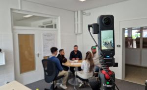 Insta360-Kamera auf Ulanzi-Stativ filmt vier Personen an einem runden Tisch in einem hellen Raum.