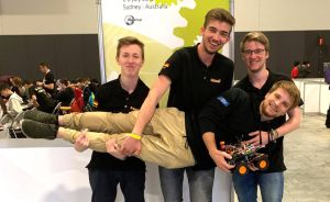 Vier junge Männer in schwarzen Shirts beim RoboCup 2019 in Sydney; drei tragen einen vierten, der einen Roboter hält.