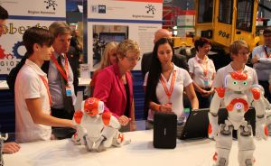 Mehrere Personen betrachten kleine humanoide Roboter an einem Messestand der Region Hannover.