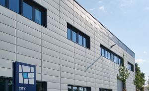 Modernes Bürogebäude „City Dock Hannover Ost, Nr. 100" mit grauer Metallfassade, Parkplatz und Behindertenstellplatz.