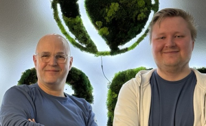 Zwei Männer mit verschränkten Armen vor grüner Mooswand-Dekoration in Form einer Weltkugel.