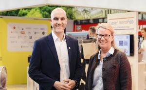 Zwei Personen stehen lächelnd vor einem Messestand mit der Aufschrift „Hannover" und „Laser nanoFab".