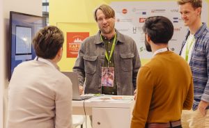 Vier Personen im Gespräch an einem Messestand von „Skando Energie" mit Monitor und Informationsmaterialien.