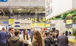 Messestand „Hannover" mit Besuchergruppen in Halle 15. Schilder u.a. „Inleap Photonics" und „The Länd" sichtbar.
