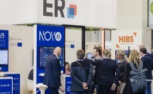 Messestand mit "NOVAI"- und "HIBS"-Logos auf der Hannover Messe; mehrere Personen stehen davor und unterhalten sich.