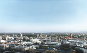 Luftaufnahme einer mitteleuropäischen Stadt mit Bahnhof, Kirchtürmen und historischen Gebäuden unter blauem Himmel.