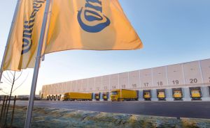 Continental-Flaggen vor einem Logistikzentrum mit gelben LKWs an nummerierten Laderampen, blauer Himmel.