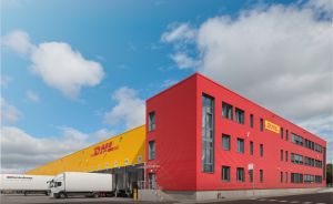 DHL-Logistikzentrum mit rotem Bürogebäude, gelbem Lagerdach und einem LKW an der Laderampe.