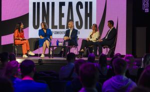 Fünf Personen sitzen auf einer Bühne vor einer Leinwand mit der Aufschrift „UNLEASH" und diskutieren vor Publikum.
