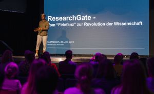 Person spricht auf Bühne vor Publikum. Hinter ihr Leinwand mit „ResearchGate – vom Firlefanz zur Revolution der Wissenschaft".