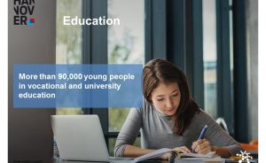 „Junge Frau schreibt an einem Tisch mit Laptop und Buch. Text: Über 90.000 junge Menschen in Berufs- und Hochschulbildung."