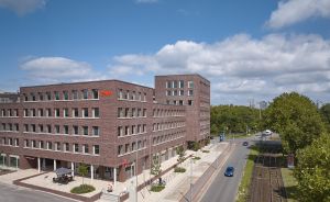 Modernes Bürogebäude aus rotem Backstein mit E.ON-Logo, neben Straße mit Straßenbahnschienen und Bäumen.