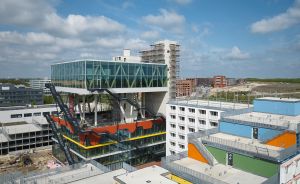 Modernes Gebäude mit Glasfassade und farbigen Elementen in einer Stadtentwicklungszone, umgeben von Baustellen.