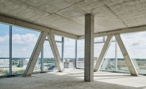 Rohbau eines Hochhauses: Betondecke, -säulen und diagonale Stützen, großflächige Glasfronten mit Stadtblick.