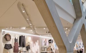 Modernes Bekleidungsgeschäft mit geometrischen Betonstützen, Kleidungsstangen und beleuchteten Wanddisplays auf zwei Etagen.