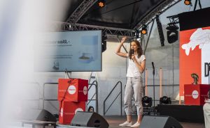 Frau auf Bühne mit Mikrofon, Präsentation „Doggy Bell" im Hintergrund, rote Hannover-Impuls-Boxen seitlich.