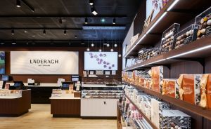 Innenansicht eines Läderach-Schokoladengeschäfts mit Holzregalen, Produkten und beleuchtetem Markenlogo an der Wand.