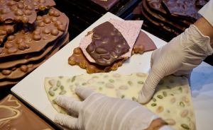 Hände mit weißen Handschuhen arrangieren verschiedene Schokoladentafeln (dunkel, rosa, weiß mit Nüssen) auf weißem Tablett.