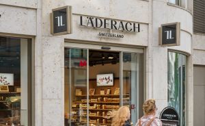Zwei Frauen gehen an einem Läderach-Schokoladengeschäft in der Schweiz vorbei. Schaufenster mit Produkten sichtbar.