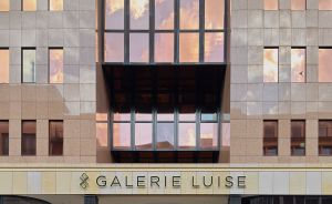 Frontansicht des Gebäudes „Galerie Luise" mit großen Glasfenstern, Steinfassade und zwei Personen am Eingang.