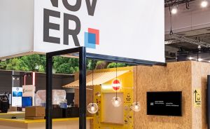Messestand mit großem „HANNOVER"-Schriftzug, weißem Tisch, Stühlen, Hängeleuchten und OSB-Holzwänden.