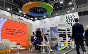 Messestand Hannover mit Schild "Energiekonzept Bahnstadt Connect to Transform Braunschweig", zwei sitzende Männer im Gespräch.