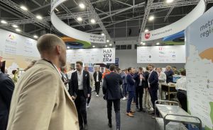 Messehalle mit Besuchern in Businesskleidung, Hannover- und Niedersachsen-Stand, Schild metropolregion.de sichtbar.