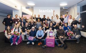 Große Gruppe von Personen posiert lächelnd vor einem "Leanlab"-Logo, einige halten Blumen und Urkunden.